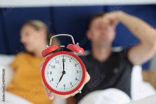Red alarm clock against the background of a sleeping couple