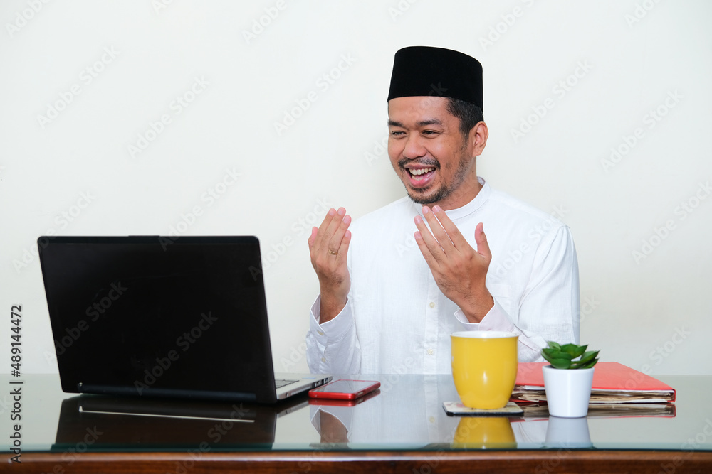 Moslem Asian man showing grateful gesture when looking to his laptop Moslem Asian man showing grateful gesture when looking to his laptop