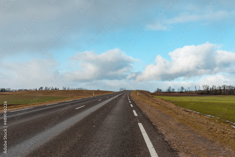 Empty road asphalt landscape among green spring meadows , blue sky,white clouds.