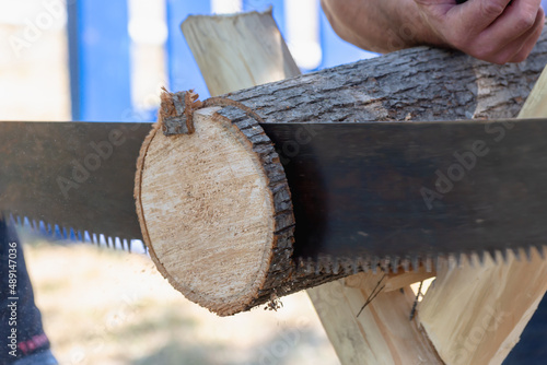 Firewood is being cut on the frame with a hand saw.