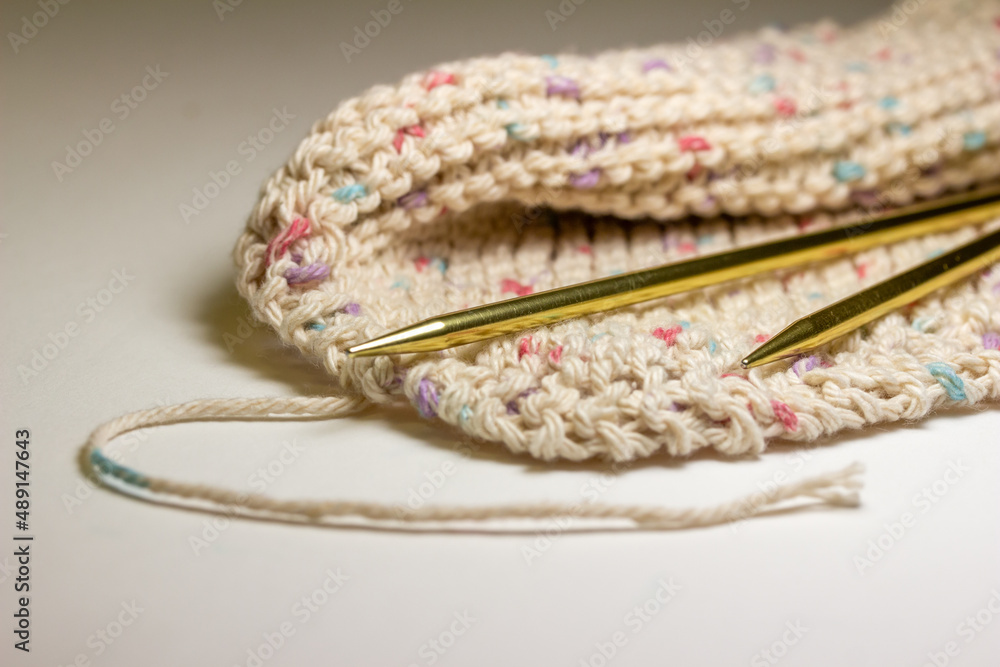 Close-up defocused view of a hand-knitted cotton wash cloth and a pair of metal knitting needles on white background, with copy space Close-up defocused view of a hand-knitted cotton wash cloth and a pair of metal knitting needles on white background, with copy space