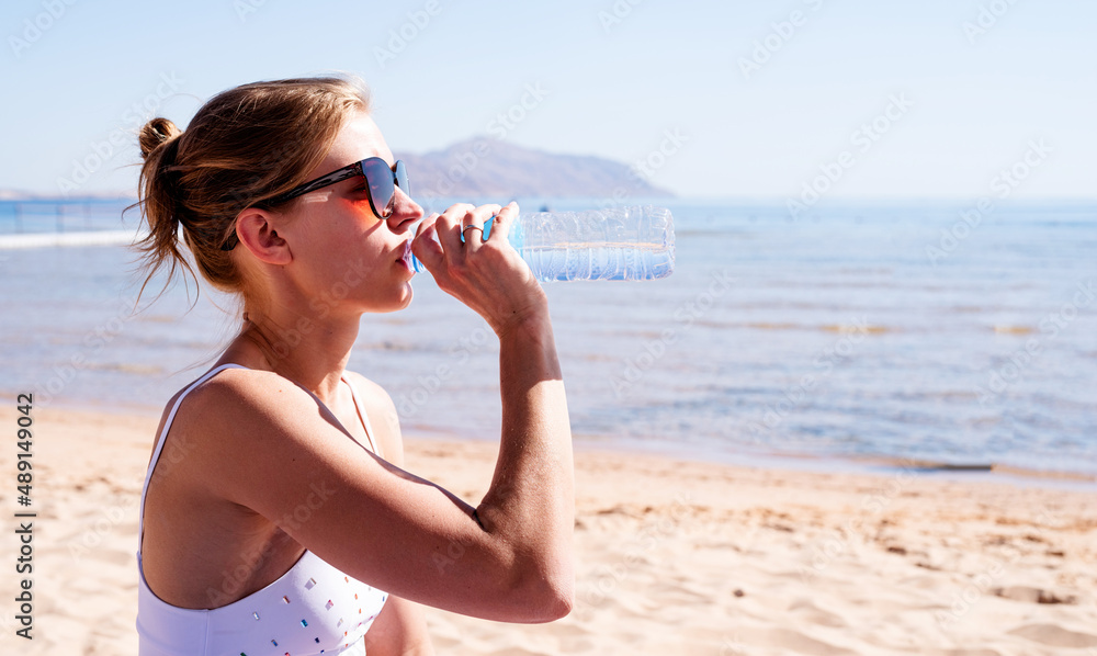 Naklejka premium beautiful woman wearing sunglasses drinking water on the tropical beach