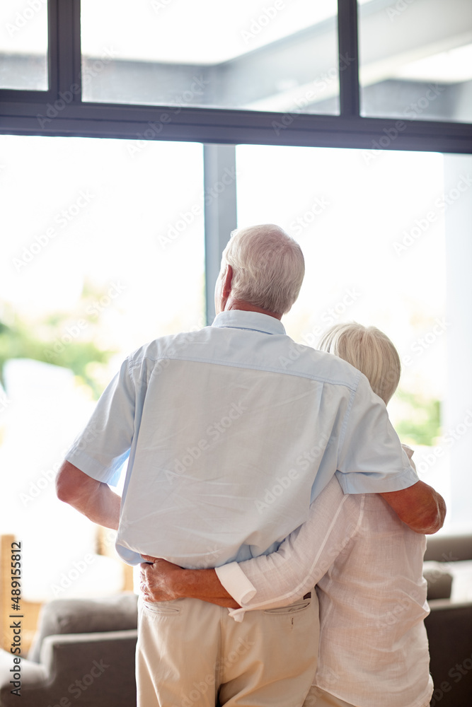 We did good. Rearview shot of a senior couple looking through their living room window. We did good. Rearview shot of a senior couple looking through their living room window.