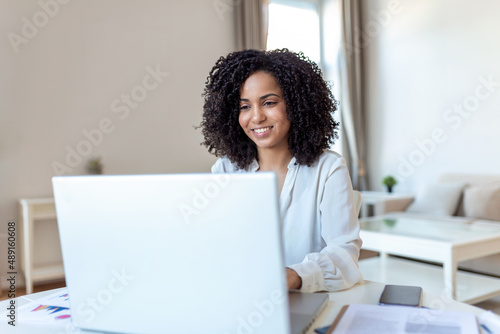 Remote job, technology and people concept - happy smiling young business woman with laptop computer and papers working at home office during the Covid-19 health crisis.
