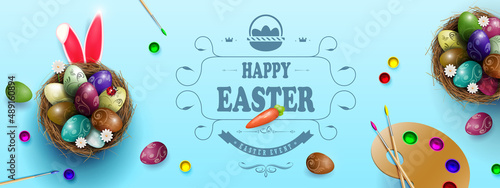 Blue composition with Easter eggs in nests, rabbit ears, palette with paints