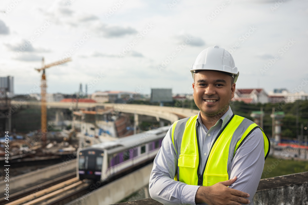 Asian engineer man or architect looking forward with white safety helmet in city construction site . Standing on rooftop building construction at capital.