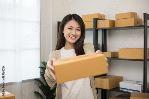 Beautiful young asian entrepreneur standing pose smiling to camera. Female small Business owner with box working at home. Startup freelance people with many parcel on background.