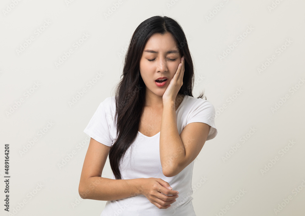 Asian woman puts her hand on her mouth and feels toothache because of tooth decay. Problems with teeth bad breath. Asian woman around 25 standing on isolated background Asian woman puts her hand on her mouth and feels toothache because of tooth decay. Problems with teeth bad breath. Asian woman around 25 standing on isolated background