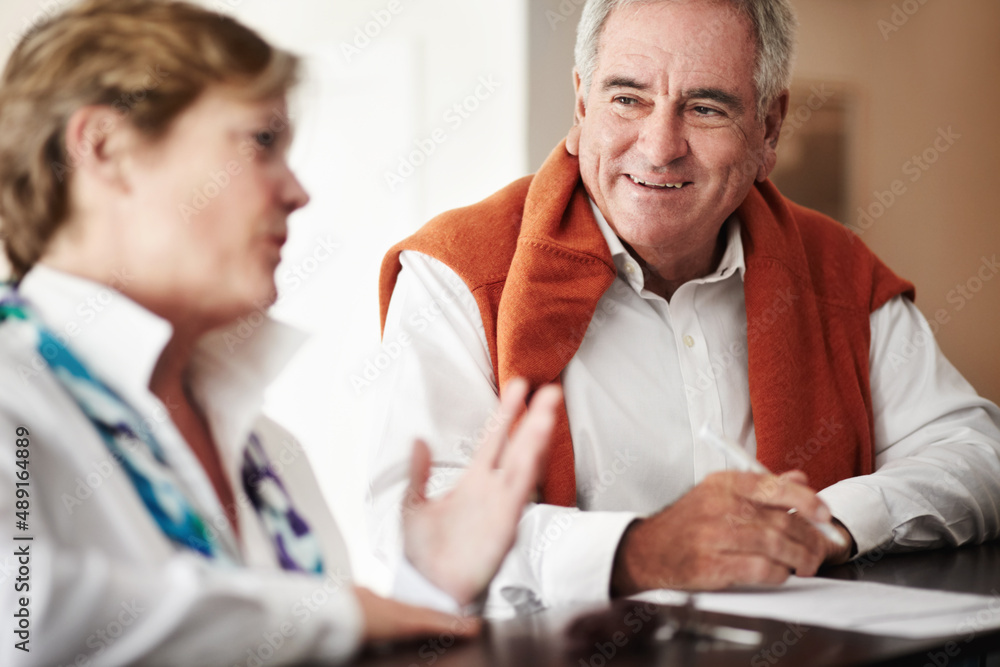 Enjoying a conversation at the reception desk. A senior man and his wife filling out forms at a hotel reception desk. Enjoying a conversation at the reception desk. A senior man and his wife filling out forms at a hotel reception desk.