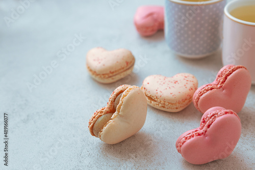 Macarons or French macaroons in heart shapes and two cups on gray background with copy space