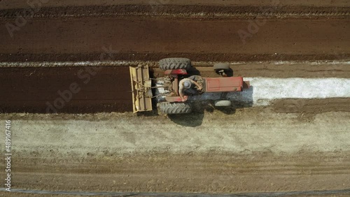Red tractor plowing the field and furrowing in a plantation, agronomics concept, cenital rising drone shot