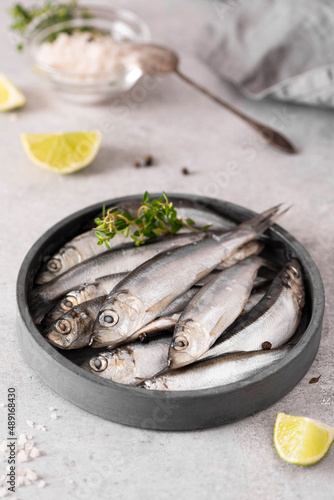 fresh large sprats with lemon, herbs and sea salt on a gray plate, close-up