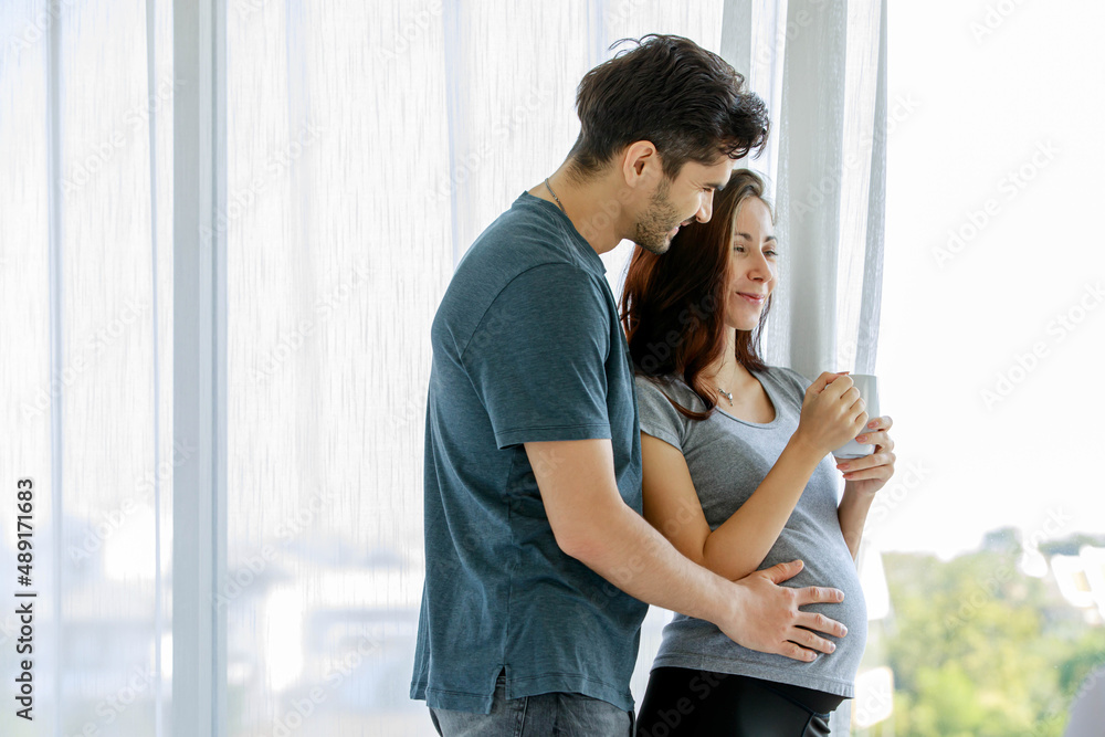Father tenderly embracing beloved wife and touching belly of unborn baby while motherhood drinking glass of milk for pregnancy nourishment Father tenderly embracing beloved wife and touching belly of unborn baby while motherhood drinking glass of milk for pregnancy nourishment