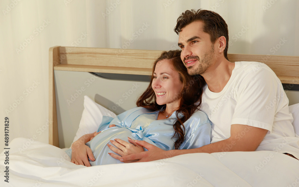 Cheerful pregnant wife smile and happy as beloved husband give love by warm hug on belly of unborn baby and adore her maternity Cheerful pregnant wife smile and happy as beloved husband give love by warm hug on belly of unborn baby and adore her maternity