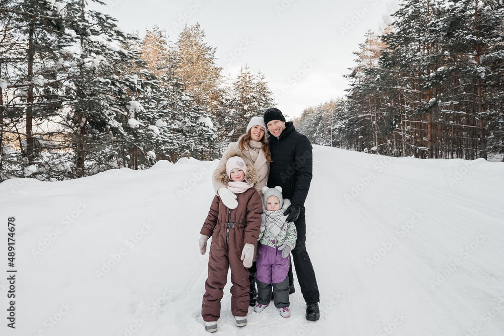 dad and mom and two daughters walk through the snowy forest