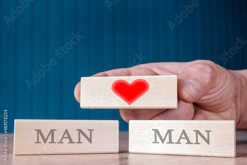 a man's hand holds a wooden block on which a red heart is drawn.