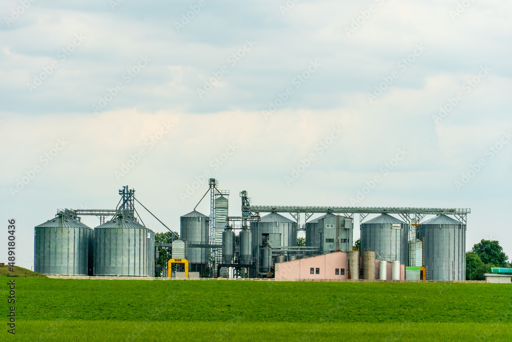 A large modern plant for the storage and processing of grain crops. view of the granary on a sunny day against the blue sky. End of harvest season. silver silos on agro manufacturing plant A large modern plant for the storage and processing of grain crops. view of the granary on a sunny day against the blue sky. End of harvest season. silver silos on agro manufacturing plant