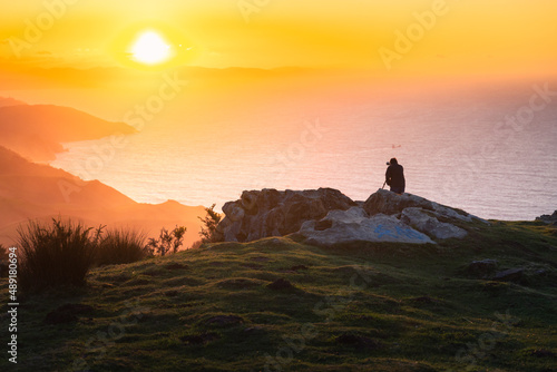 Photographer silhouette taking photos on the top of Jaizkibel mountain at sunset.
