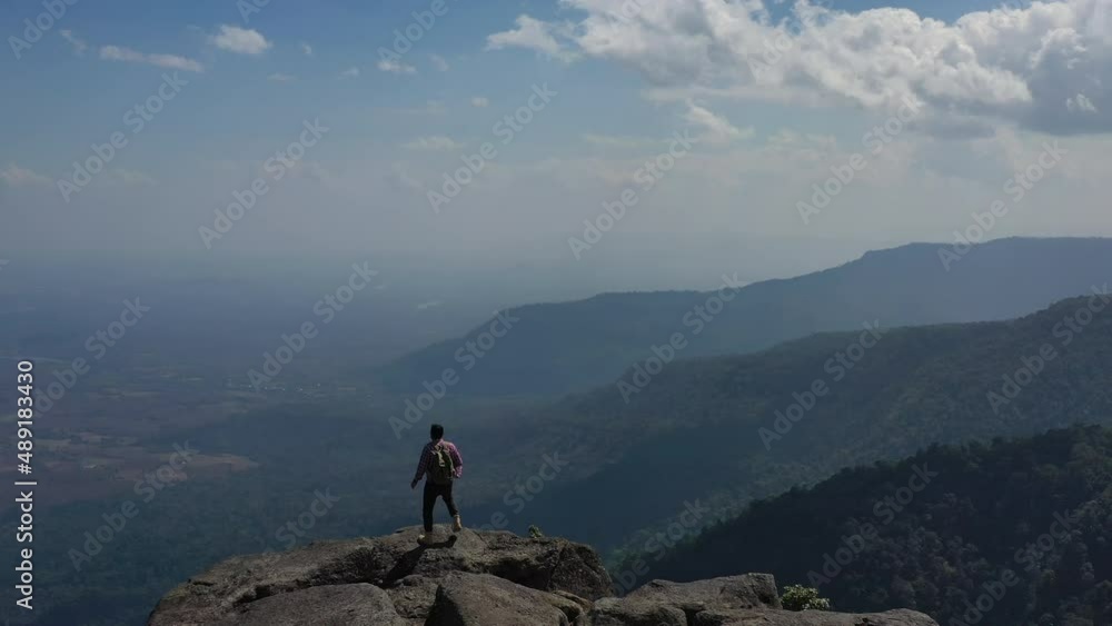 Aerial drone view, Rear view Young hiking man walking and rise-up hands with happy on peak of rocky mountain Aerial drone view, Rear view Young hiking man walking and rise-up hands with happy on peak of rocky mountain