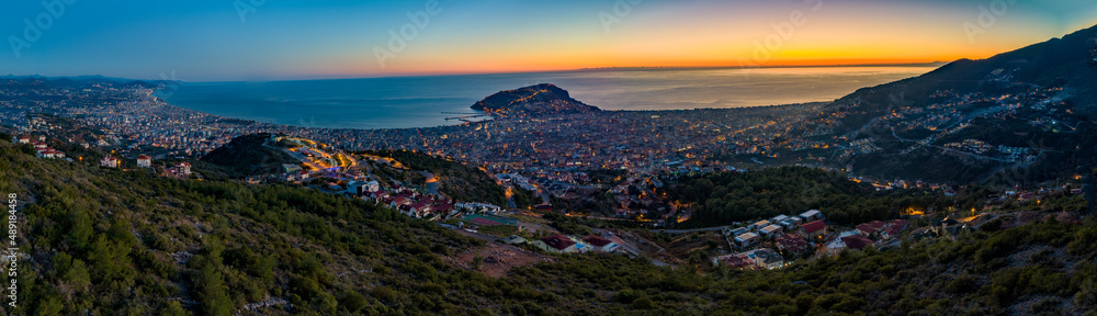 Aerial Panoramic view of Alanya City at Twilight - Alanya Castle & Peninsula in the center of the frame, Beautiful Sky, City lights and endless Mediterranean Sea