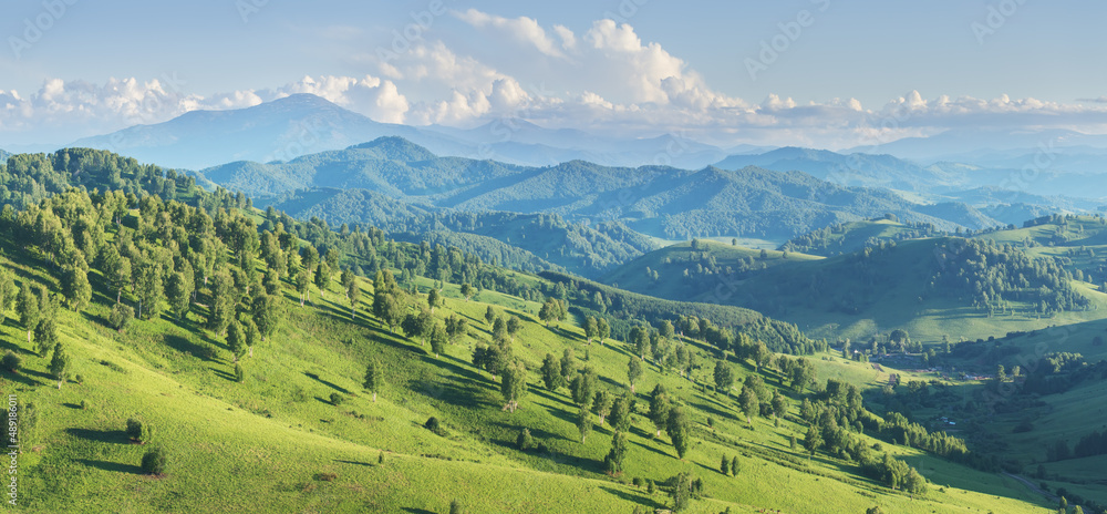 Picturesque valley, panoramic mountain view. Bright sunlight, spring greens of forests and meadows.