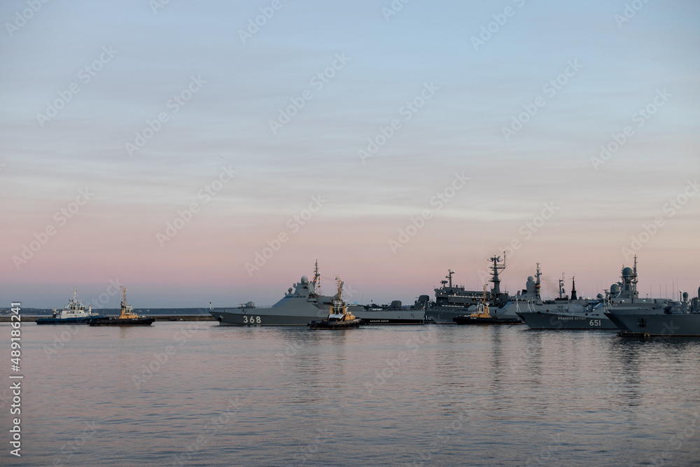 Two naval harbor tugs against the background of warships in the Petrovskaya pier of Kronstadt. Evening sunset. Russia, Kronstadt, July 26, 2020
