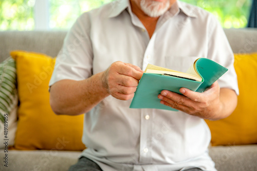 Close up asian elderly man reading book at home after retirement.