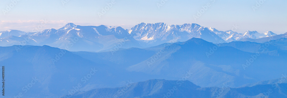 Fototapeta premium Mountains in blue haze, panoramic view. Peaks in the clouds, valley and mountainsides.