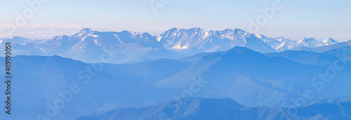 Mountains in blue haze, panoramic view. Peaks in the clouds, valley and mountainsides.