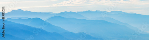 Mountains in blue haze, panoramic view. Peaks in the clouds, valley and mountainsides. © Valerii