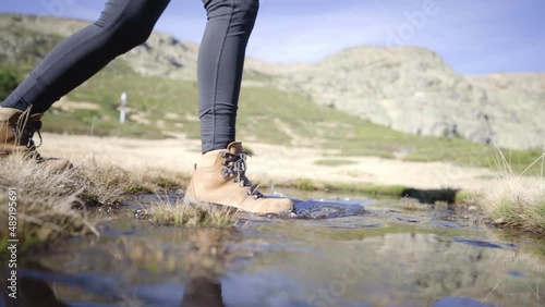 Madrid Penalara park Spain, slow motion of trekker wearing waterproof shoes crossing water river bed on a mountain path adventure trail photo