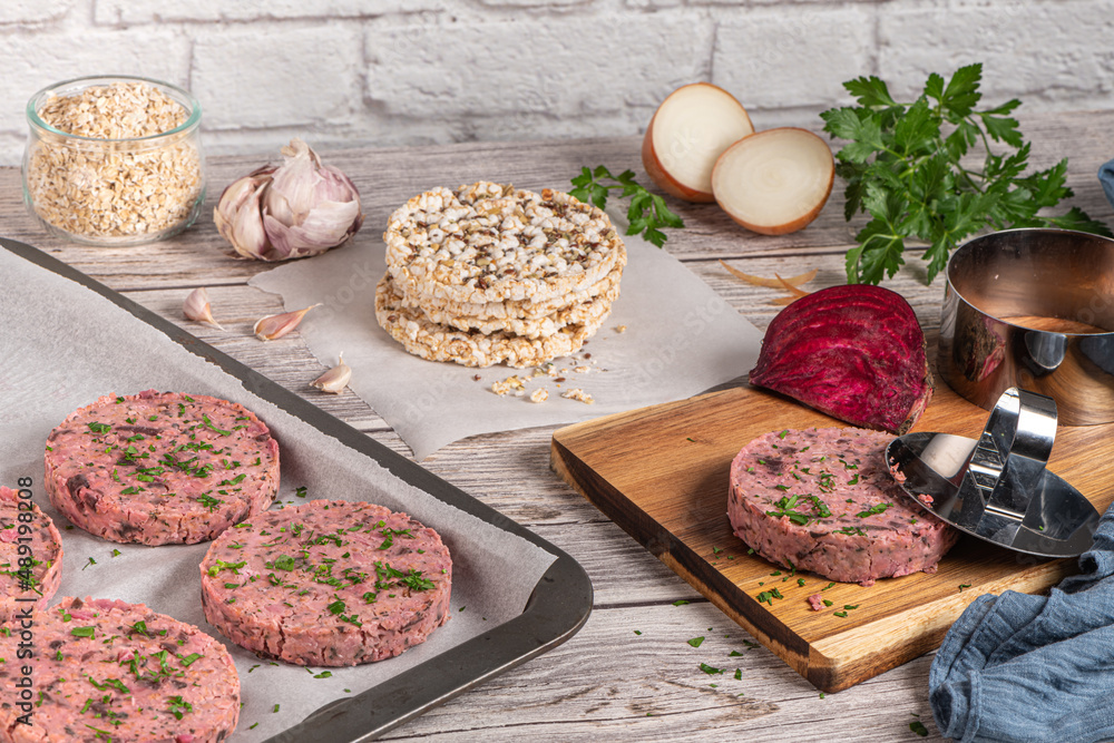 Raw veggie burger with beetroot and white beans with parsley leaves on wood cutting board.