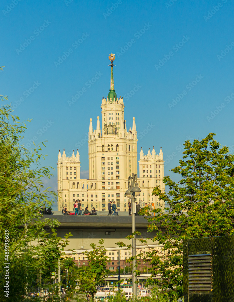 Moscow, Russia, June 16, 2019: View of Stalinist skyscraper on Kotelnicheskaya Embankment in rays evening sun. People stroll along floating bridge on background of Stalinist skyscraper. Moscow, Russia, June 16, 2019: View of Stalinist skyscraper on Kotelnicheskaya Embankment in rays evening sun. People stroll along floating bridge on background of Stalinist skyscraper.