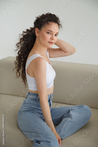 A cute slender girl sits on a sofa on a light background.