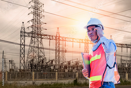 A picture of an electrical engineer holding a smartphone and a notebook computer standing at the power station to watch the planned work by generating electrical power at the high-voltage electrodes. photo