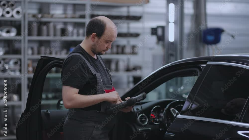 Car diagnostics. A mechanic in a close-up car service holds a tablet in his hands and presses the screen near the car Car diagnostics. A mechanic in a close-up car service holds a tablet in his hands and presses the screen near the car