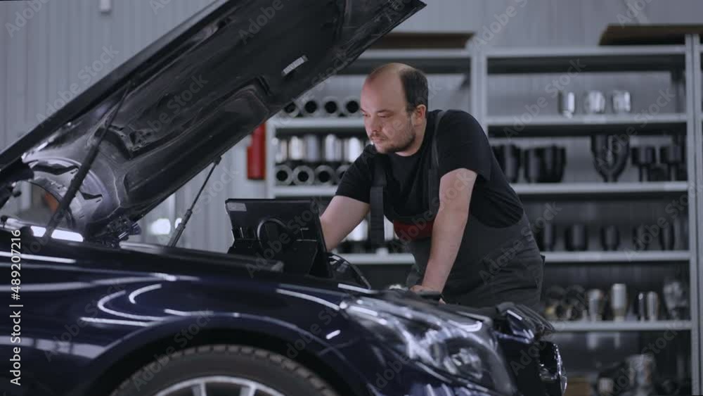 Auto mechanic working with car diagnostic tool in a repair shop. Car Service Manager or Mechanic Uses a Tablet Computer with a Futuristic Interactive Diagnostics Software. Auto mechanic working with car diagnostic tool in a repair shop. Car Service Manager or Mechanic Uses a Tablet Computer with a Futuristic Interactive Diagnostics Software.