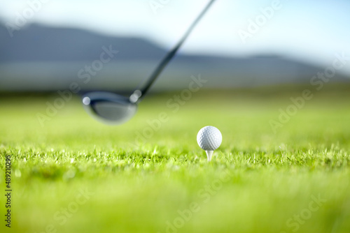 Timing the shot. A golf club ready to tee-off with a white ball on a golf course.