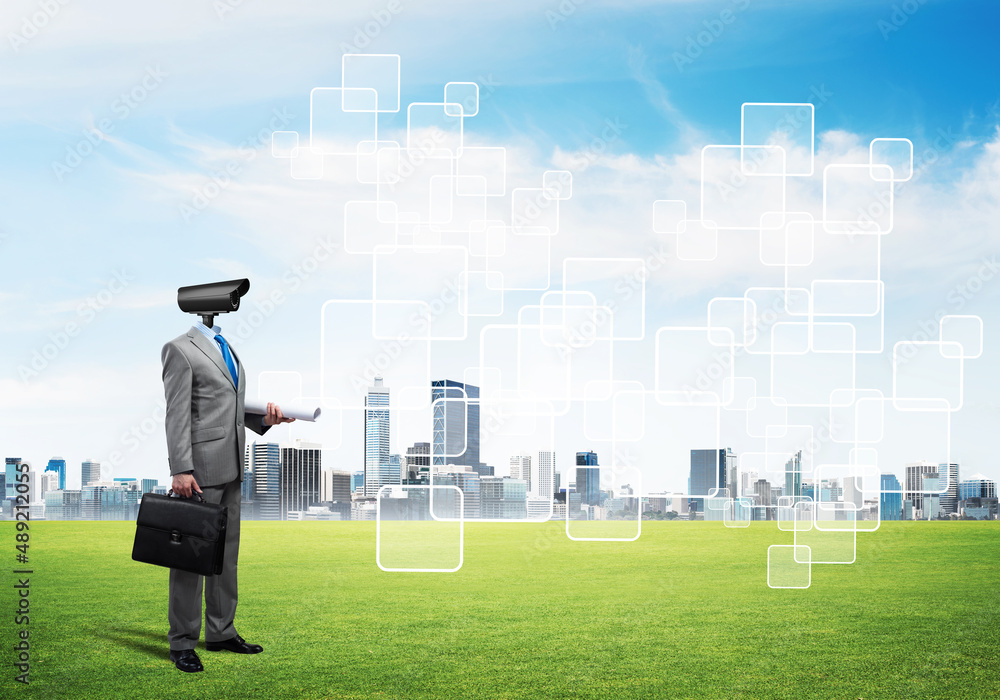 Camera headed man standing on green grass against modern cityscape