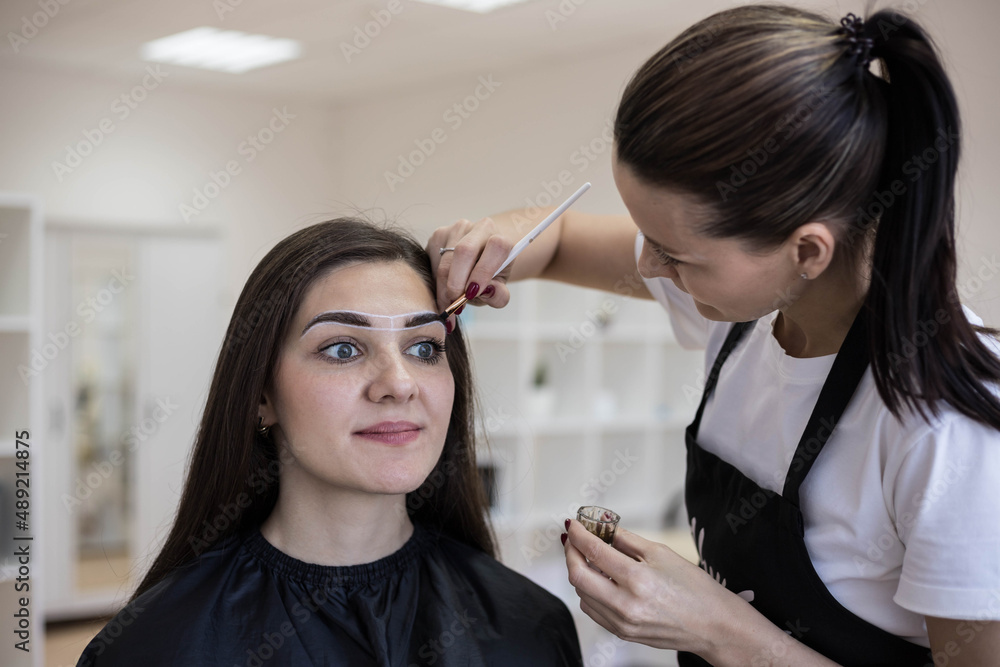 The master in the salon, after correcting the shape of the eyebrows, applies a coloring compound (paint or henna) to the eyebrow hairs.Creating beautiful eyebrows in the salon.Self-care. The master in the salon, after correcting the shape of the eyebrows, applies a coloring compound (paint or henna) to the eyebrow hairs.Creating beautiful eyebrows in the salon.Self-care.
