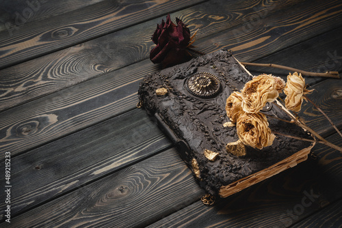 Ancient magic book and dry rose flowers on the wooden desk table close up background. photo