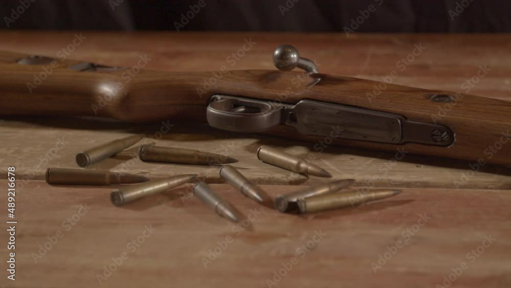 close Dolly of live ammunition lying in front of loaded WW2 era rifle on wooden surface close Dolly of live ammunition lying in front of loaded WW2 era rifle on wooden surface
