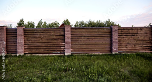 Brown wooden fence with block posts. Construction site. Corrugated surface. Private property fencing. Opaque hedge. Countryside backyard security exterior. Scandinavian, chalet or rustic style. DIY photo