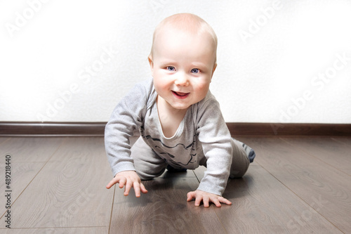 Baby boy crawling on brown floor. Happy toddler looking in camera. Copy space for text