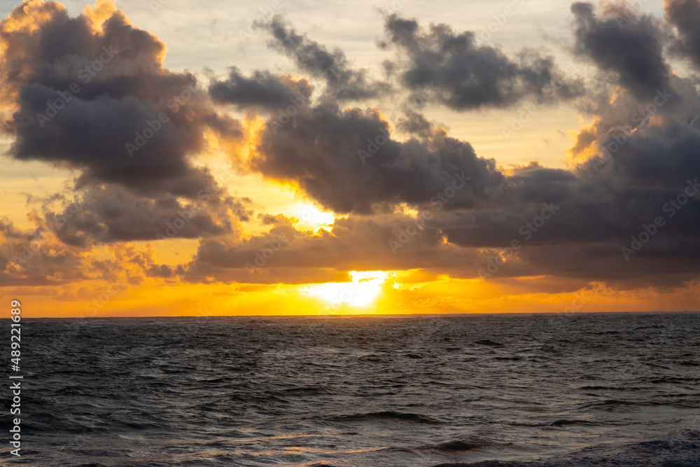 Scenic idyllic golden sunrise above the sea. Sun among clouds above the horizon water line.