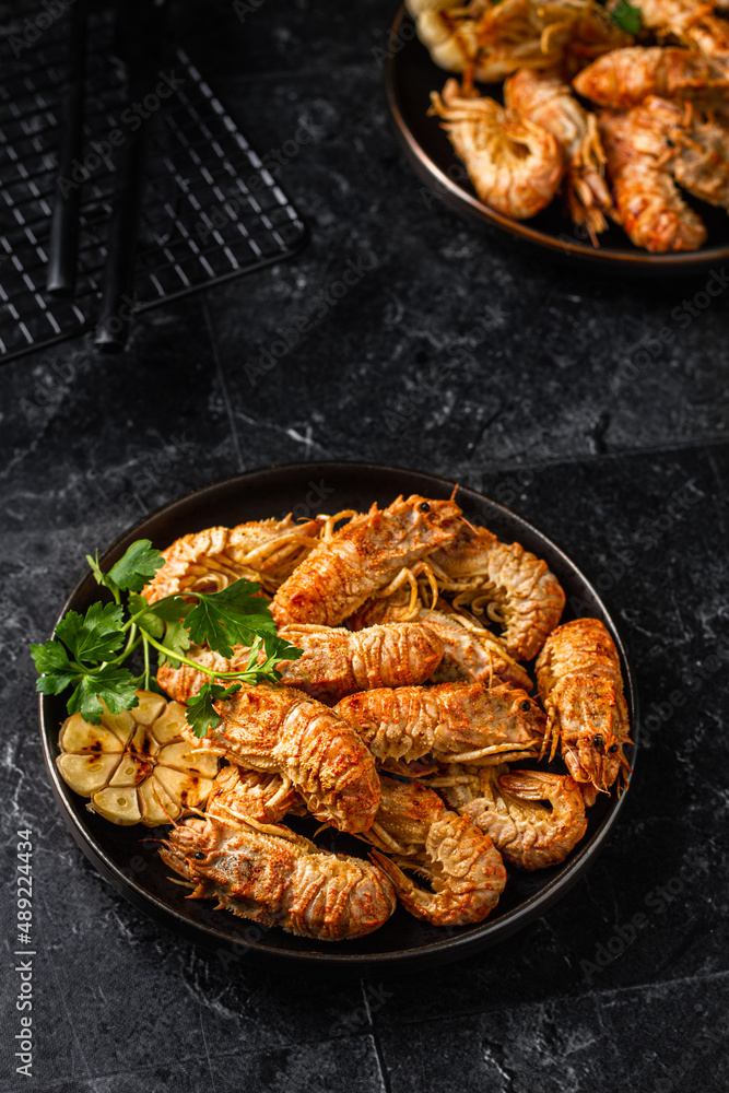 Grilled shrimp with garlic and parsley. Spiked shrimp-bear on a plate . Bering shrimp. Menu concept for restaurants. Dark photo. Grilled shrimp with garlic and parsley. Spiked shrimp-bear on a plate . Bering shrimp. Menu concept for restaurants. Dark photo.