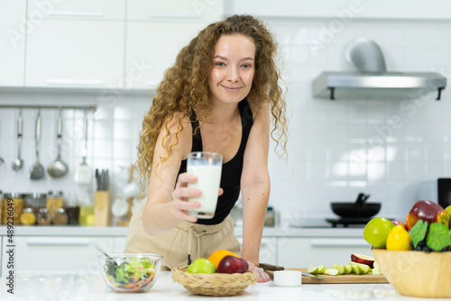 beautiful healthy woman show milk in glass, smile, happy, look at camera in kitchen with copy space. beautiful caucasian woman cooking healthy diet fruit or vegetable in kitchen