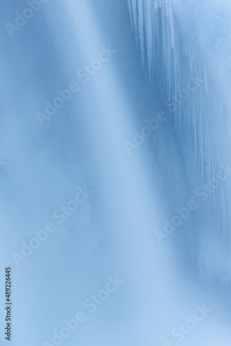 Winter landscape of a cascade captured with motion blur and framed by blue ice, Comstock Creek, Michigan, USA