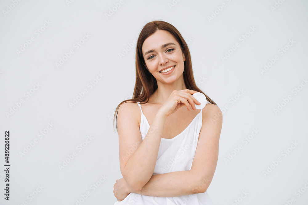 Beauty portrait of happy smiling young woman with dark long hair and clean fresh skin face with cotton pad in hand on white background isolated Beauty portrait of happy smiling young woman with dark long hair and clean fresh skin face with cotton pad in hand on white background isolated