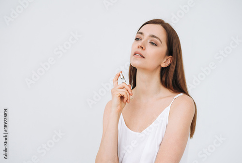 Beauty portrait of happy smiling woman with dark long hair with perfume on clean fresh skin face and hands on white background isolated